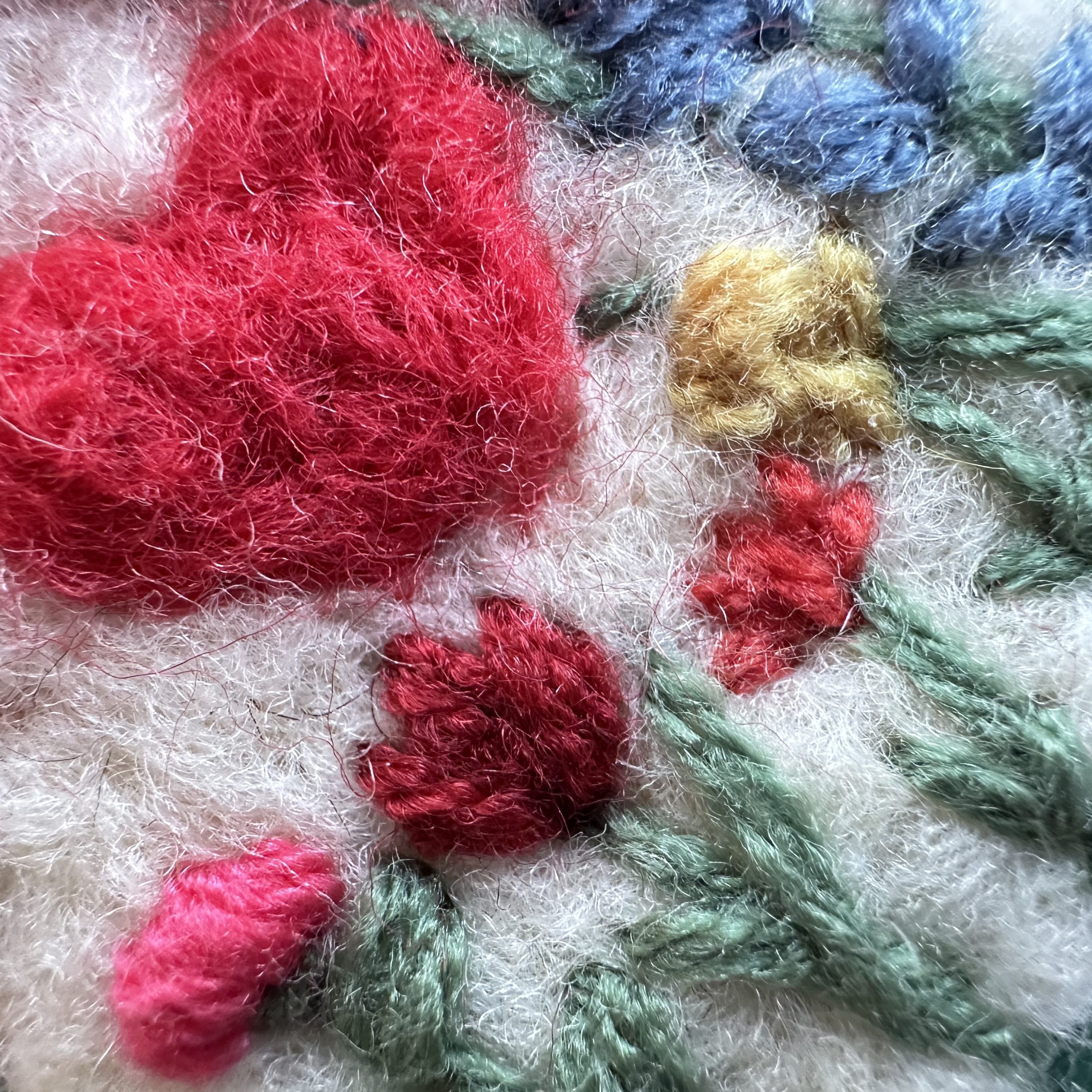 Близък макро план на червено сърце и цветя, създадени чрез сухо плъстене, показващ меката текстура на непредената вълна.